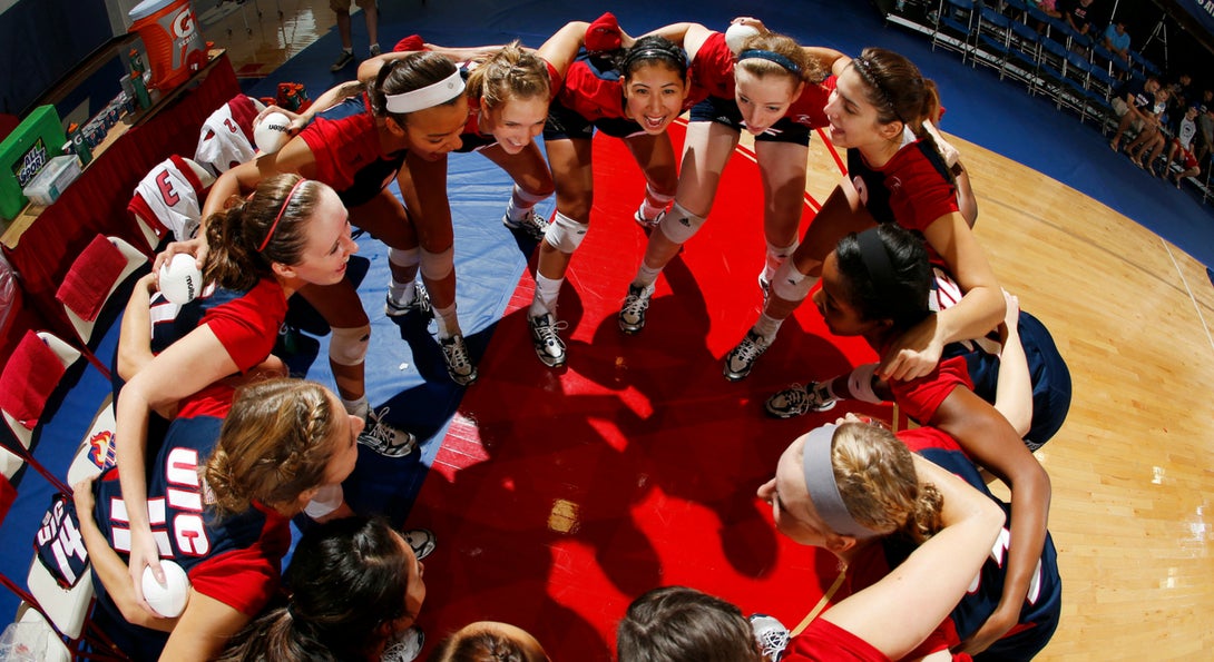 female volleyball players huddle in a circle before a game